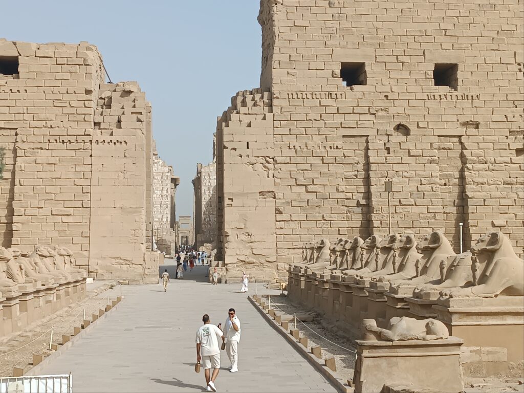 Zwei Touristen spazieren am beeindruckenden Weg der Sphingen im Karnak-Tempel während ihres Hurghada Ausflug nach Luxor.