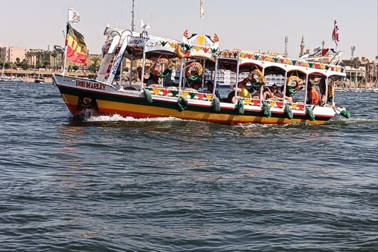 Touristen auf einem Boot auf dem Nil während ihres Hurghada Ausflug nach Luxor – im Hintergrund die Tempel von Luxor.