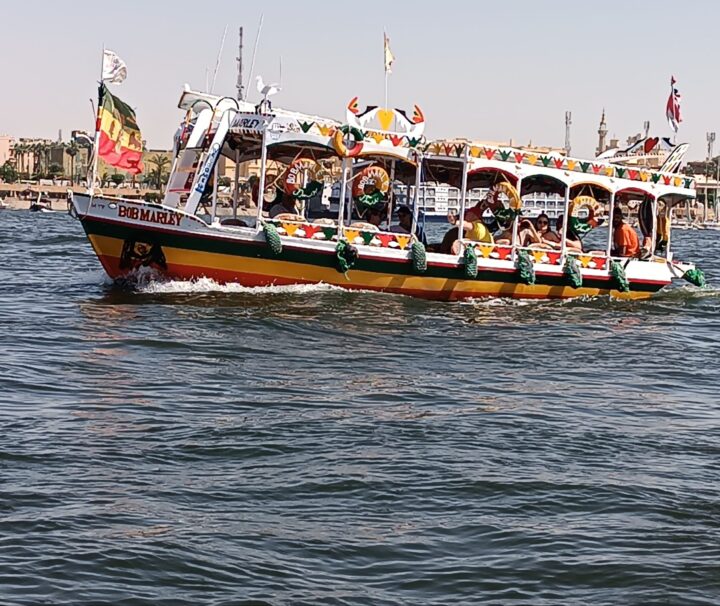 Touristen auf einem Boot auf dem Nil während ihres Hurghada Ausflug nach Luxor – im Hintergrund die Tempel von Luxor.